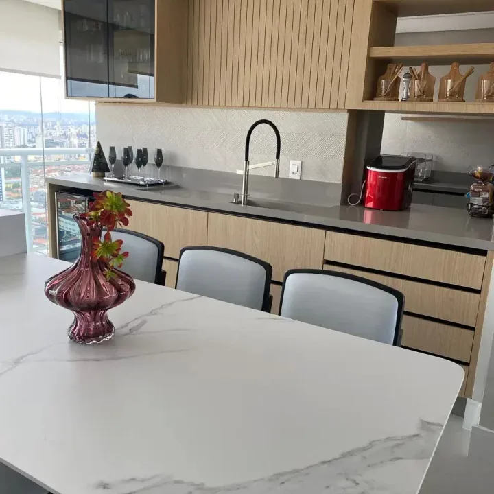 Área gourmet com ilha em mármore branco e marcenaria clara
